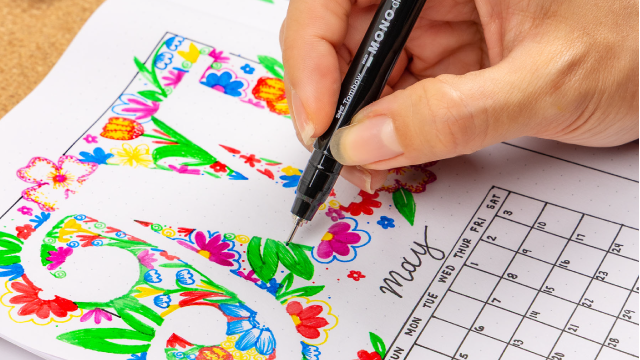 Image of markers on a flat table with an instruction book that's being colored in